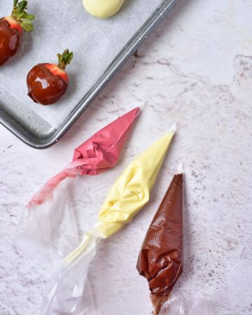 Piping bags filled with melted chocolate to make the drizzle on milk chocolate covered strawberries.