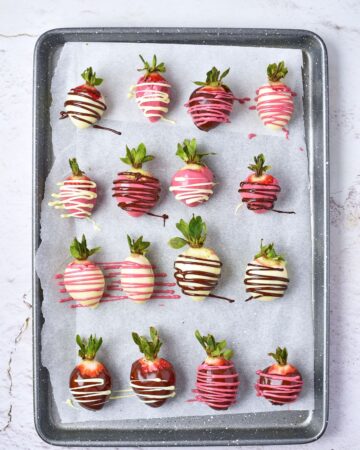 A large baking sheet with chocolate covered strawberries with colored chocolate drizzle on the strawberries.