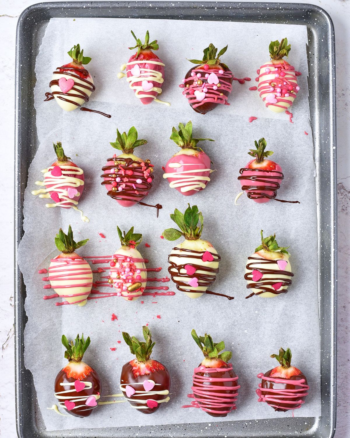 A baking tray with strawberries drizzled in chocolate and and drizzles of chocolate on a baking tray.