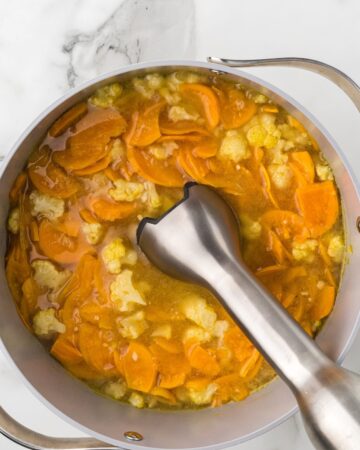 A soup pot with the ingredients for cauliflower sweet potato soup being blended together. 