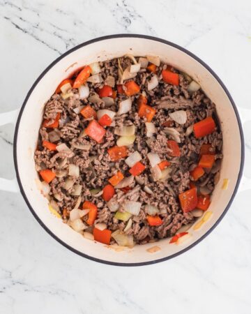 Ground beef, onions, and peppers being browned to make macaroni and cheese mac and cheese.