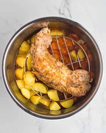 An Instant Pot vessel with potatoes and carrots with a Pork Tenderloin on a vessel to be roasted.