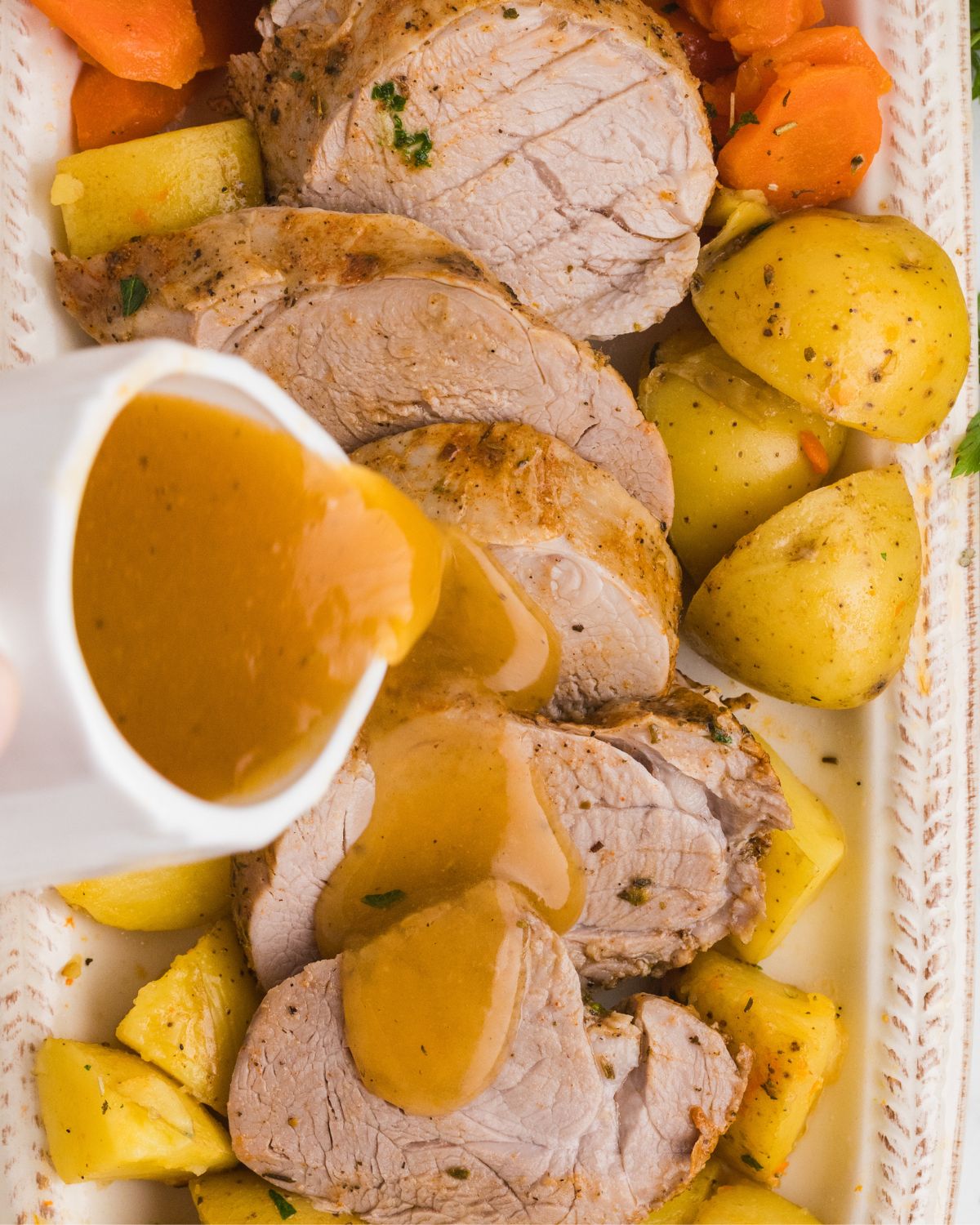 Sliced pork tenderloin with a gravy being poured over the meat.