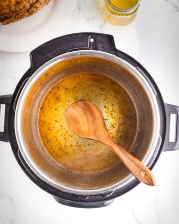 Brown bits being picked up by a wooden spoon in an Instant Pot.