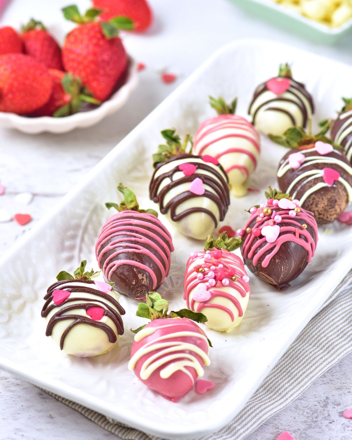 A white tray with strawberries covered with white chocolate and cocoa chocolate drizzled with pink, white, and chocolate and decorations.
