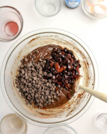 A mixing bowl with chocolate chips and cherries to make chocolate cherry brownies