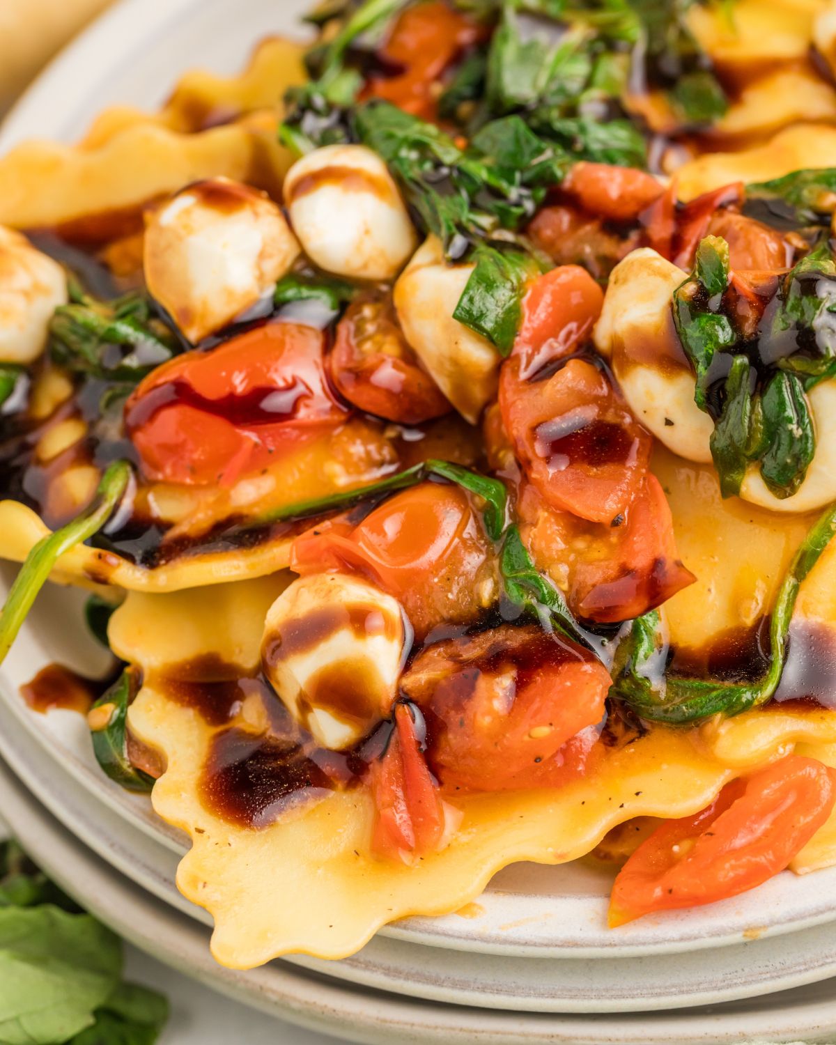 Ravioli Caprese with fresh ravioli, tomatoes, and mozzarella pearls with a balsamic glaze.