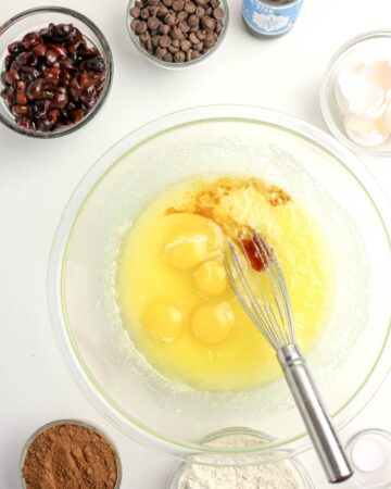 A glass mixing bowl with eggs and pure vanilla extract to make cherry brownies.