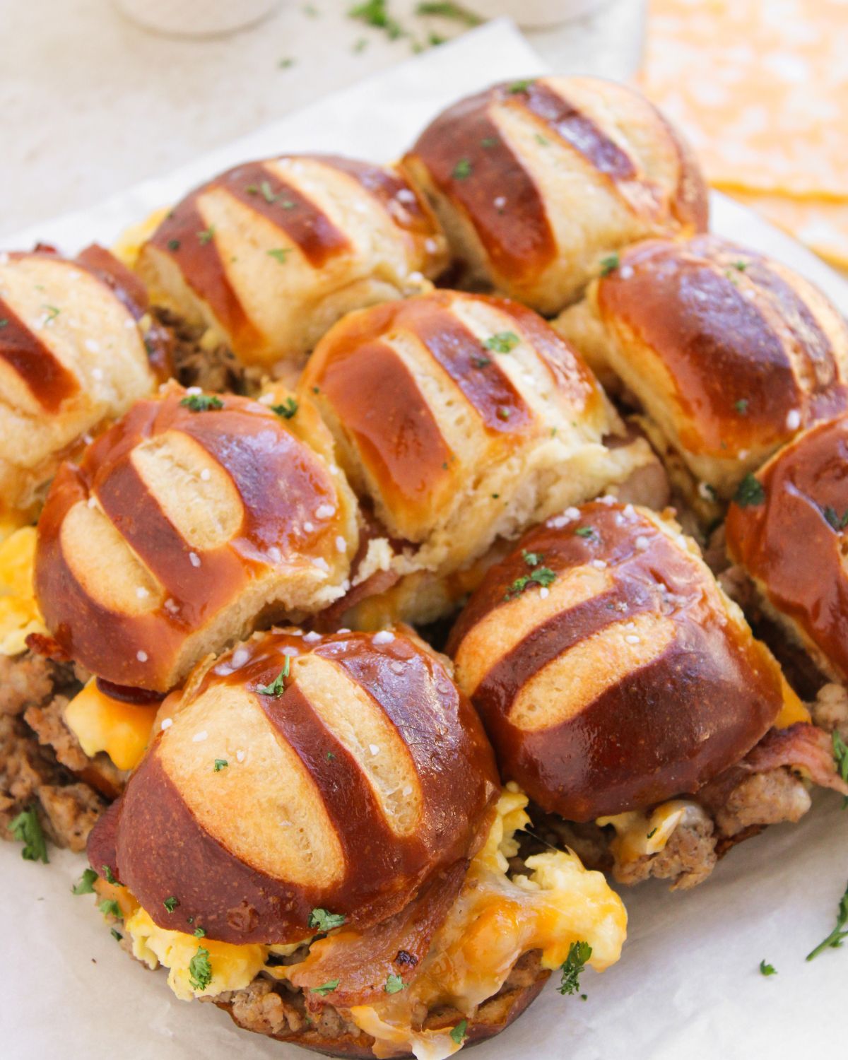 A layer of pretzel bun breakfast sliders with eggs and bacon on a plate.