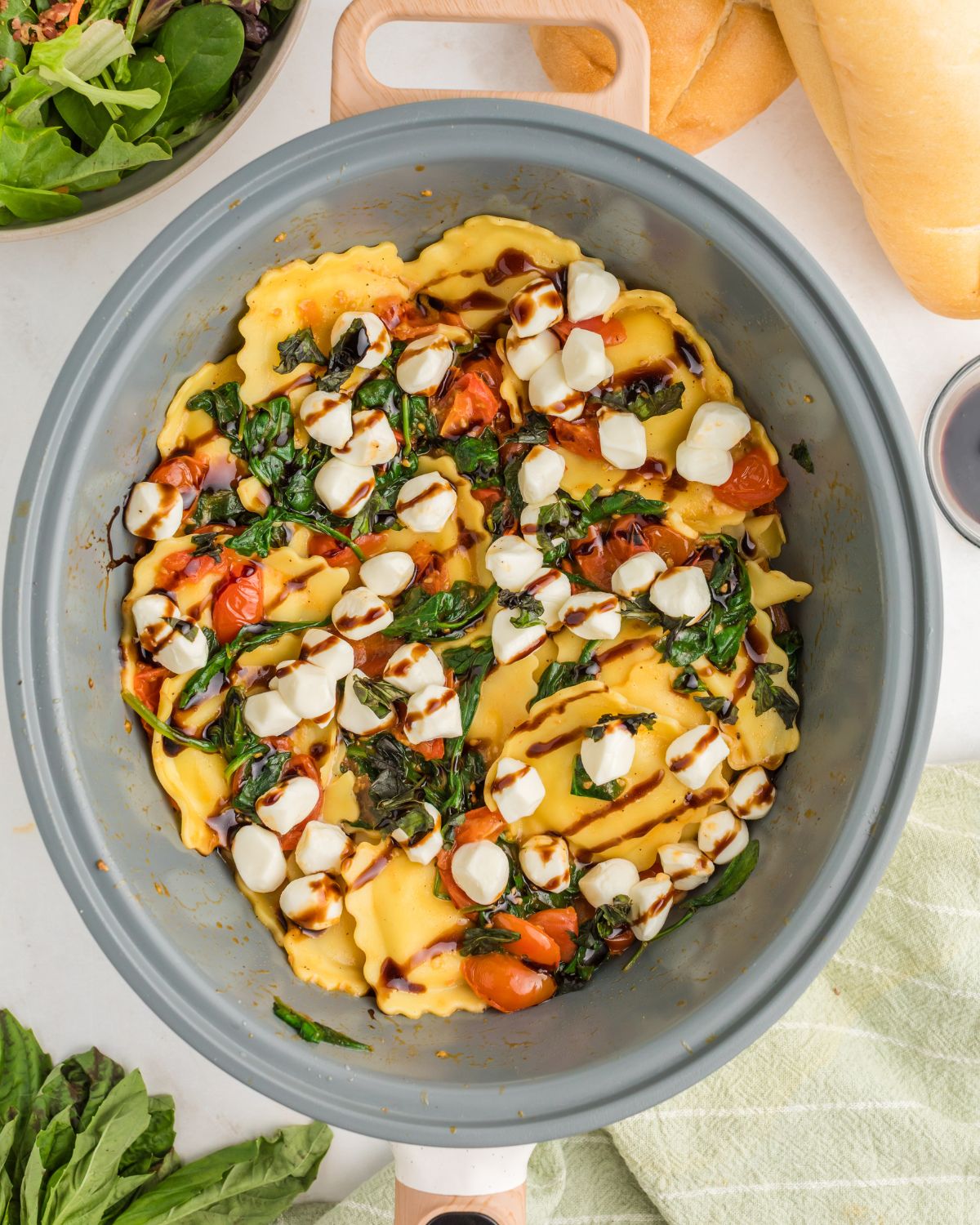 A saute pan with ravioli with a tomato and spinach sauce with mozzarella to make Ravioli Caprese.