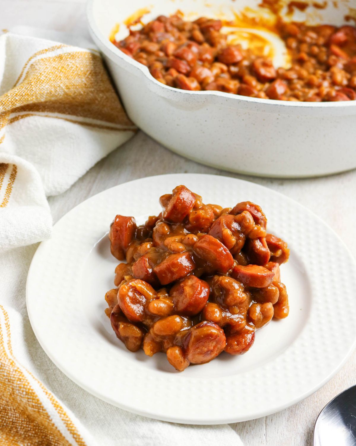 A white plate with beans and franks for a beanie weenie recipe.