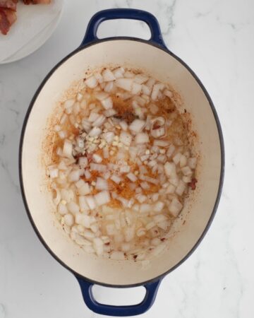 A Dutch oven with bacon fat and diced onions to make Manhattan Clam Chowder.