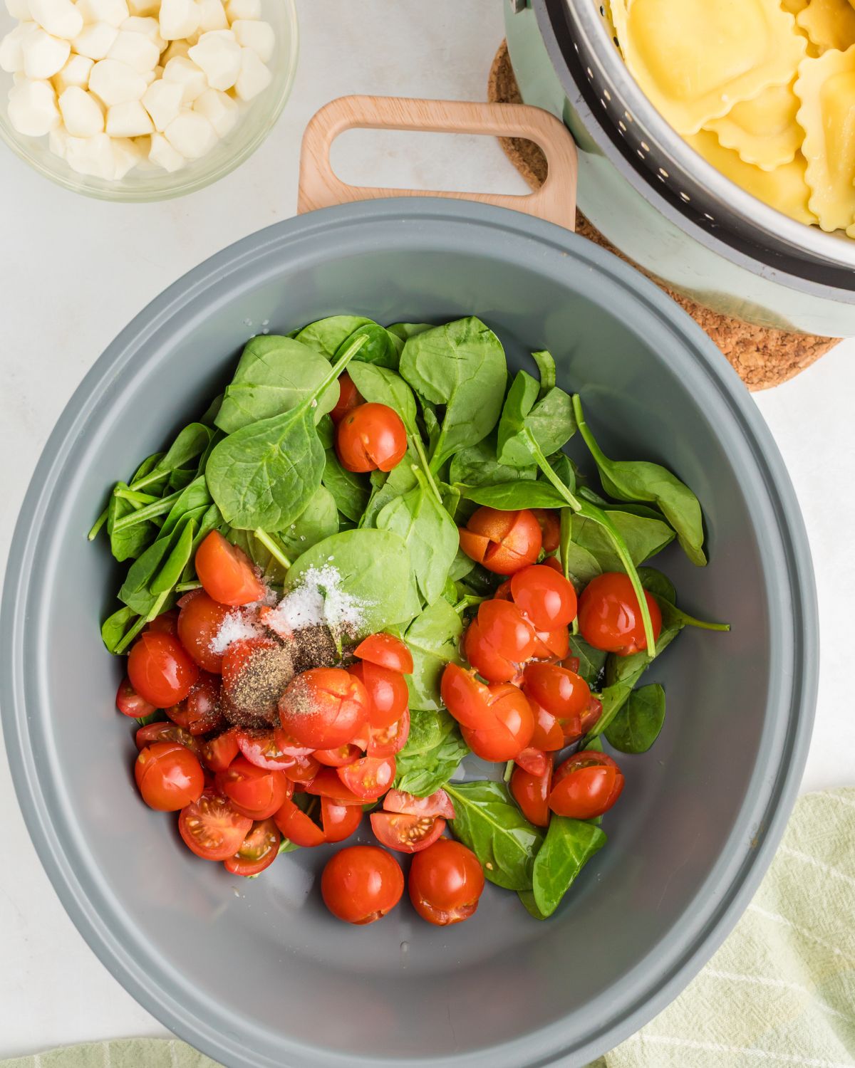 The combination of tomatoes and spinach in a dutch oven to make caprese ravioli.
