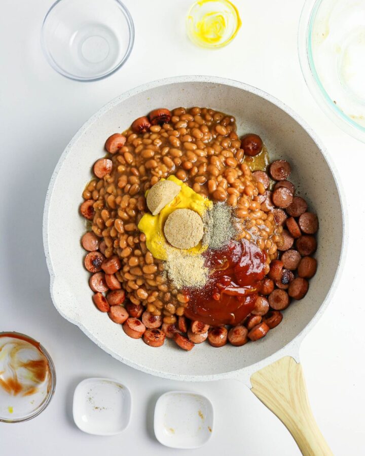 A saut&eacute; pan with beans, sliced hot dogs, mustard, and spices to make beanie weenies.