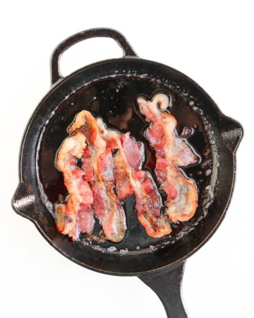 A cast iron pan with bacon cooked in the pan for breakfast sliders.