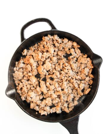 A cast iron pan with crumbled pork sausage to make breakfast sliders on pretzel buns.