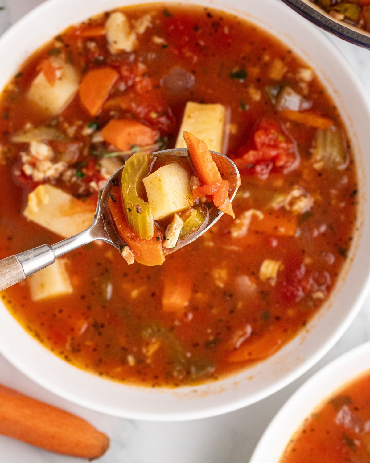 A bowl of manhattan clam chowder with a spoon picking up the chowder.