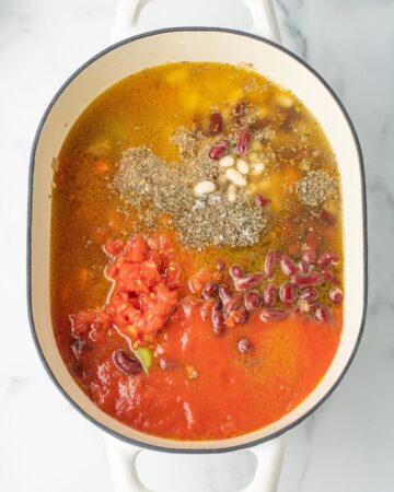 A dutch oven with navy beans, northern beans, tomato sauce, diced tomatoes, chicken stock, aromatics to make pasta e fagiole soup.