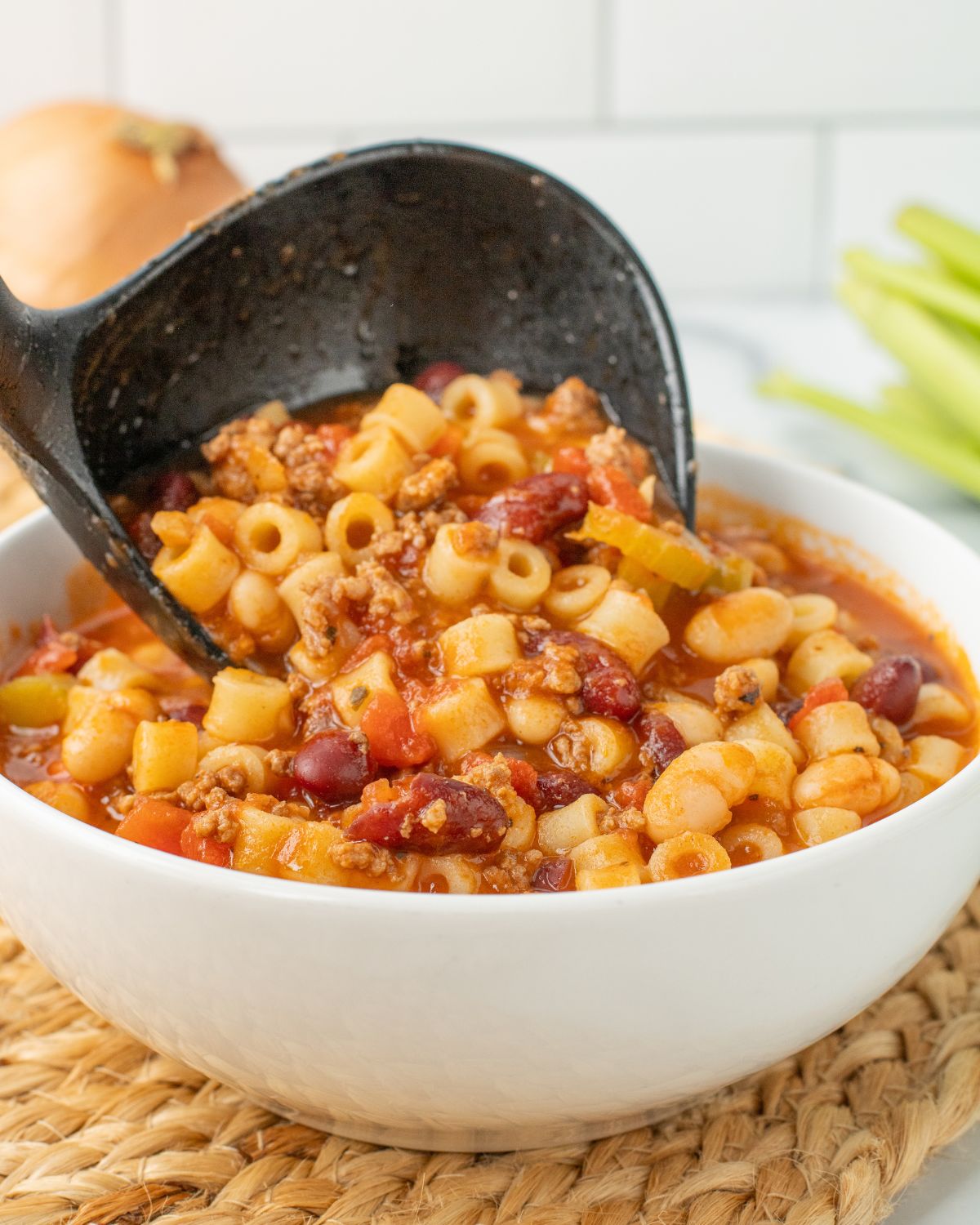A white soup bowl with a ladle serving pasta fagioli soup recipe.