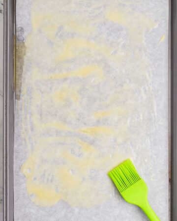 A baking sheet with melted butter to make crispy baked chicken drumsticks.