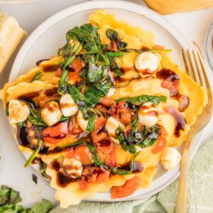 A plate of ravioli caprese with fresh ravioli, saute&eacute;d spinach and tomatoes with mozzarella.