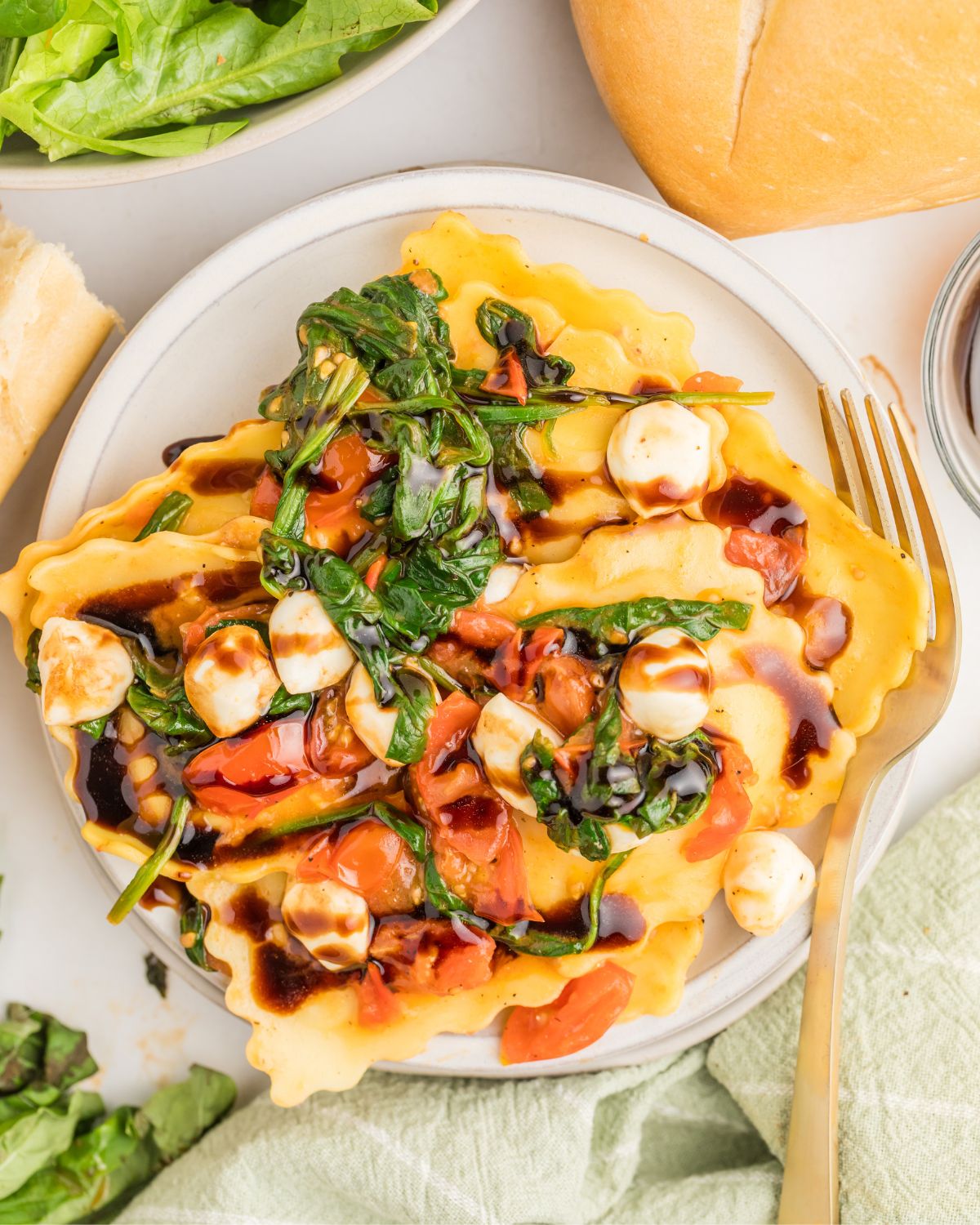 A plate of cheese ravioli topped with tomatoes, mozzarella pearls and spinach to make Caprese Ravioli.