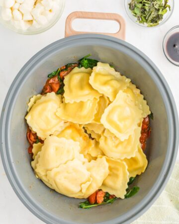 Ravioli and tomatoes and spinach in a pan to make ravioli caprese.