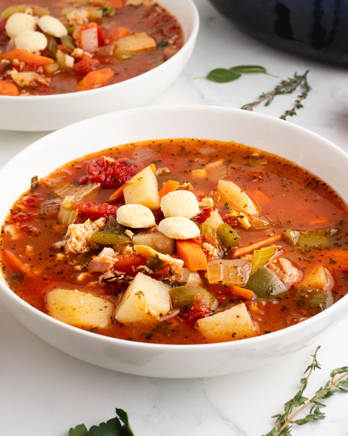 A white bowl with red Manhattan clam chowder with potatoes and vegetables with oyster crackers.