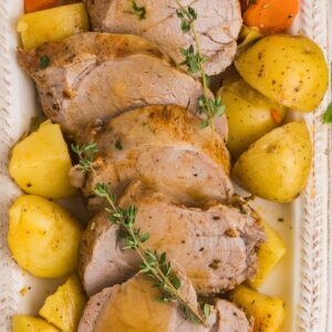 SLICED PORK TENDERLOIN WITH POTATOES MADE IN THE INSANT POT ON A WHITE PLATTER TOPPED WITH FRESH THYME.