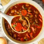 A dutch oven with Hungarian goulash and a serving spoon picking up a serving.