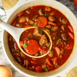 A dutch oven with Hungarian goulash and a serving spoon picking up a serving.