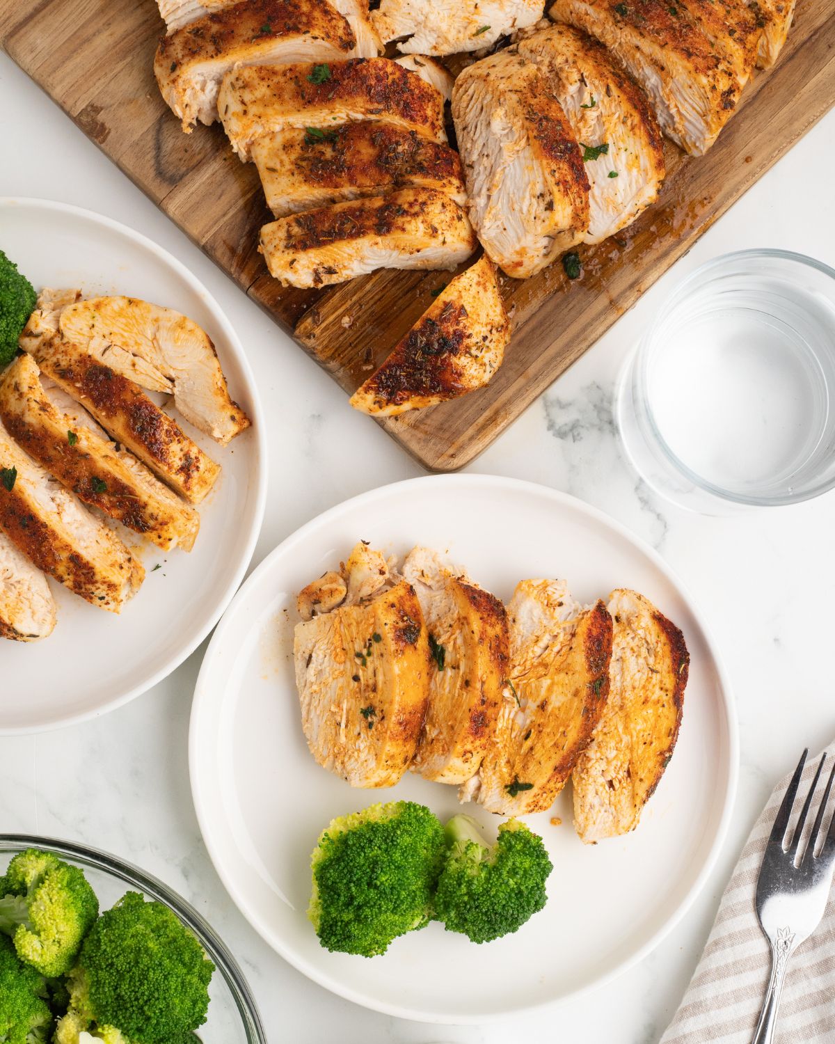 Sliced oven baked chicken breasts on a plate with roasted broccoli.
