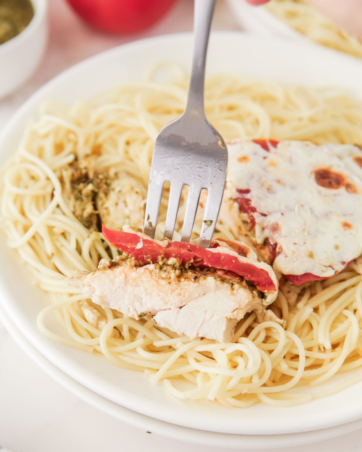 Chicken topped with tomatoes, basil pesto, and fresh mozzarella over spaghetti.