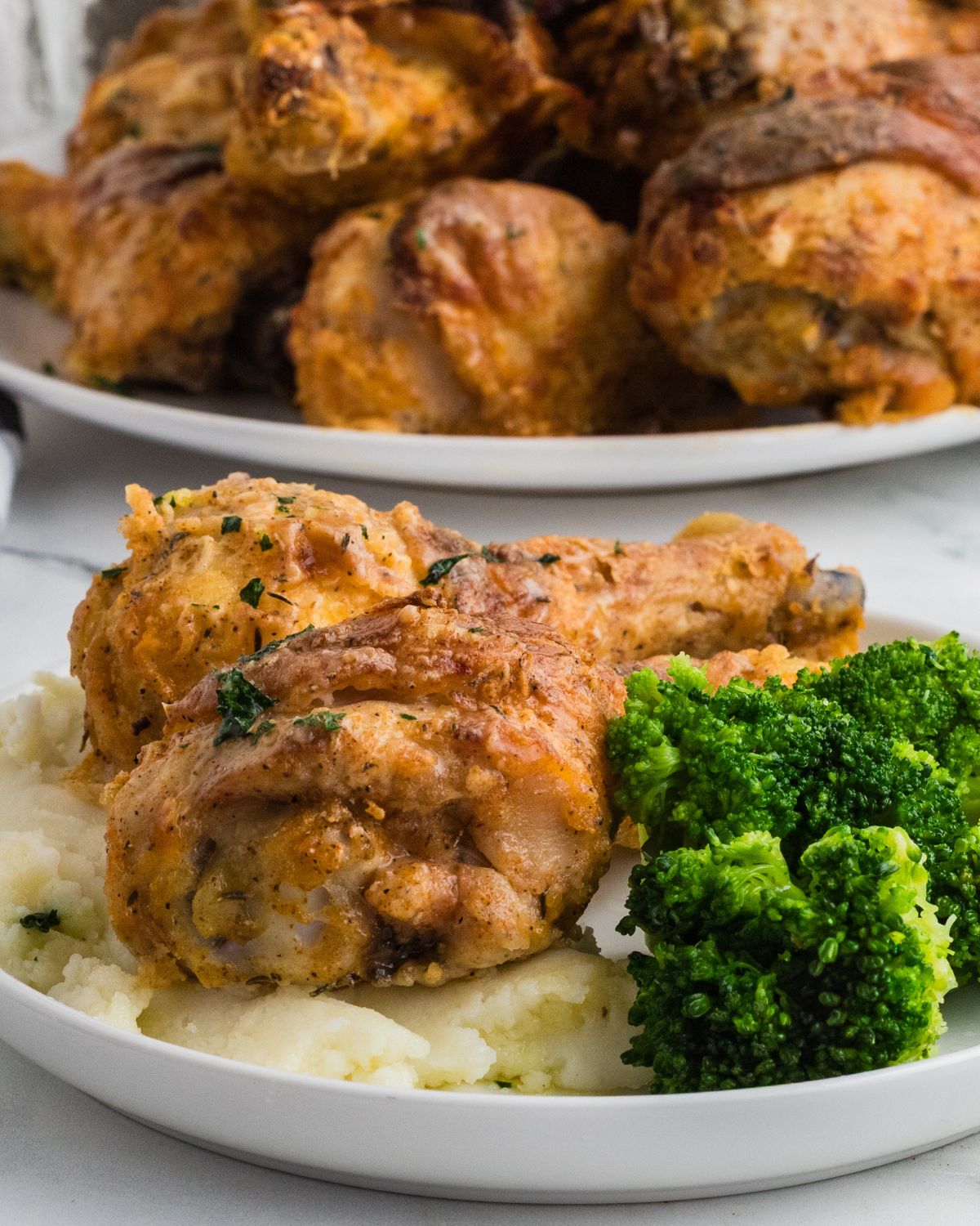 Baked fried chicken drumsticks on mashed potatoes and broccoli on the side.