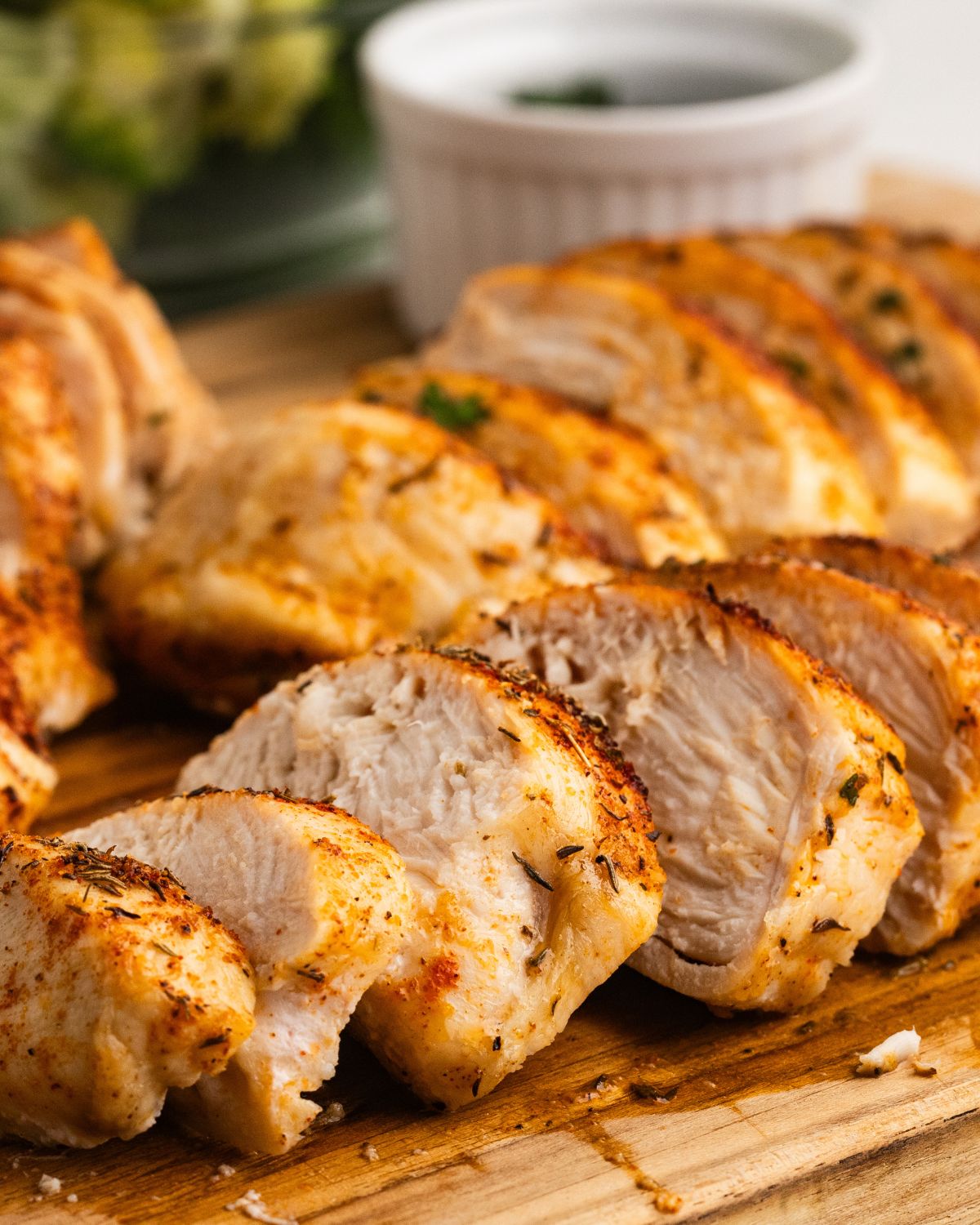 Oven baked chicken breasts with a chicken dry rub that has been sliced on a wooden cutting board.