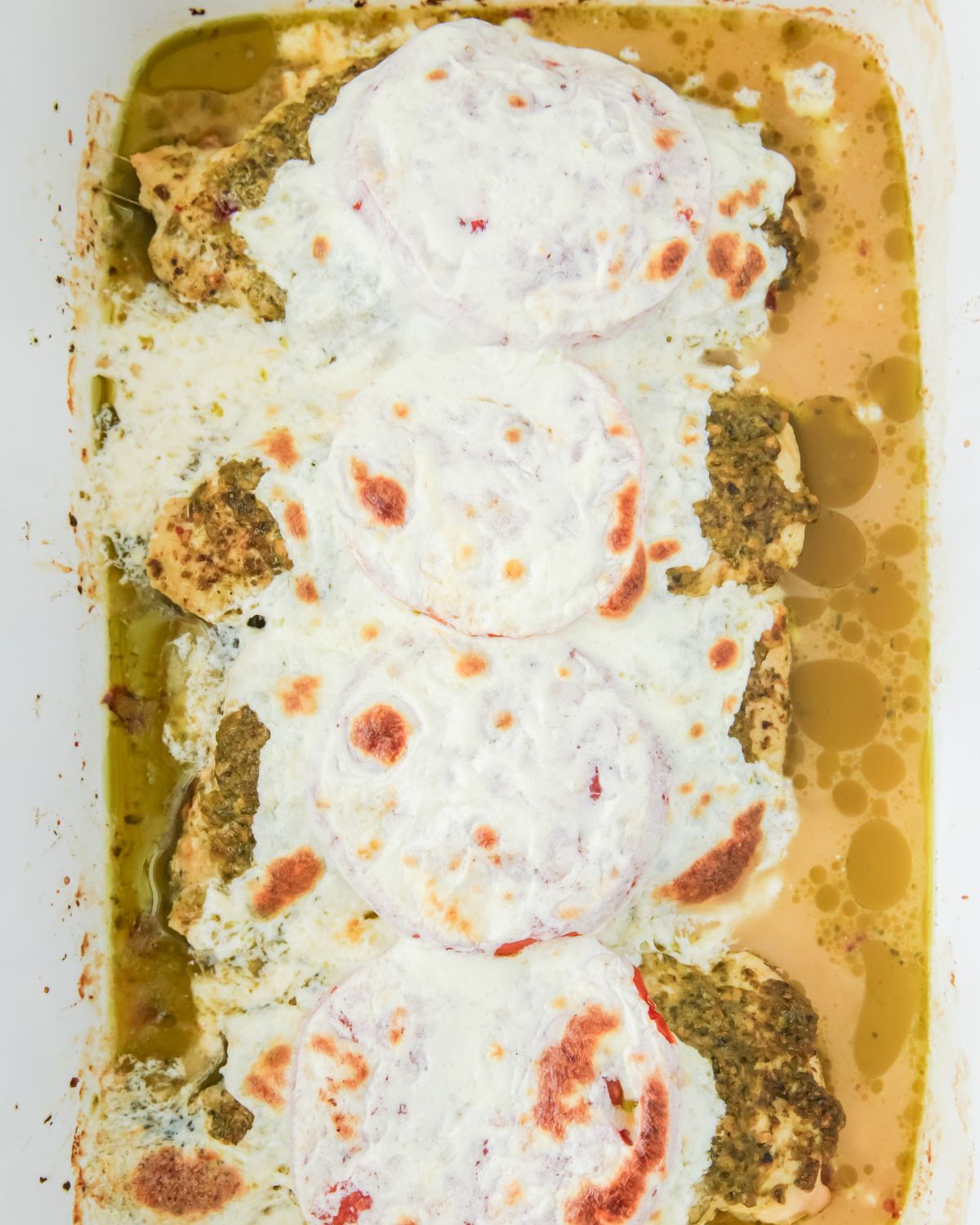 Juicy baked chicken with pesto and cheese in a baking dish. 