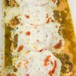 A baking dish with chicken topped with tomatoes, pesto, and fresh mozzarella.