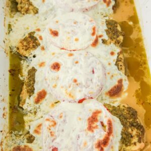 A baking dish with chicken topped with tomatoes, pesto, and fresh mozzarella.