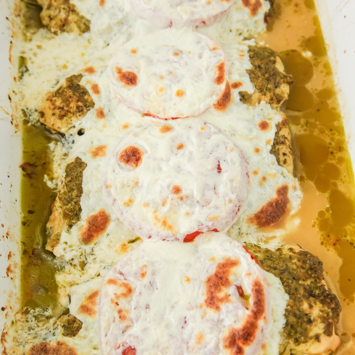 A baking dish with chicken topped with tomatoes, pesto, and fresh mozzarella.