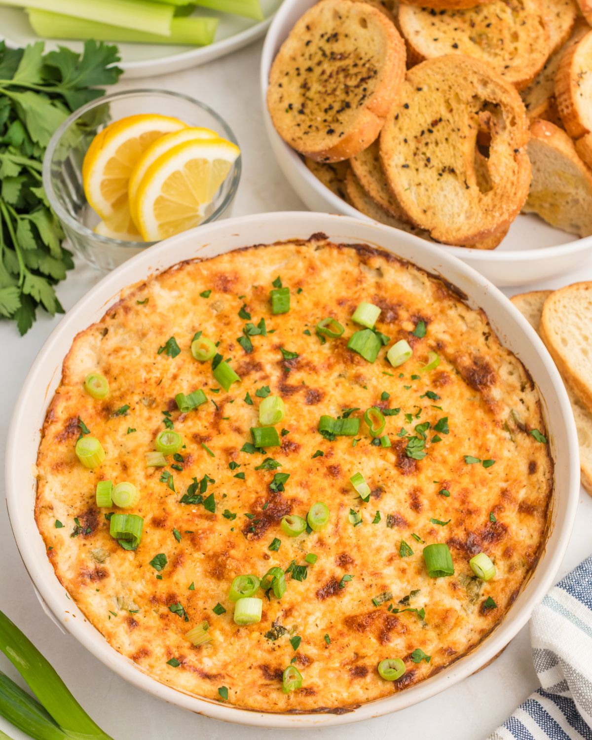 Hot crab dip in a white bowl with garlic toast and lemon on the side to dip.