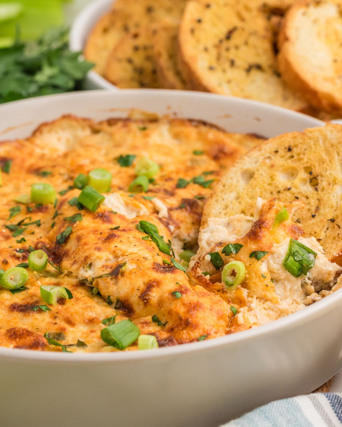 Hot Crab dip topped with chopped green onions with a slice of garlic toast in the dip.