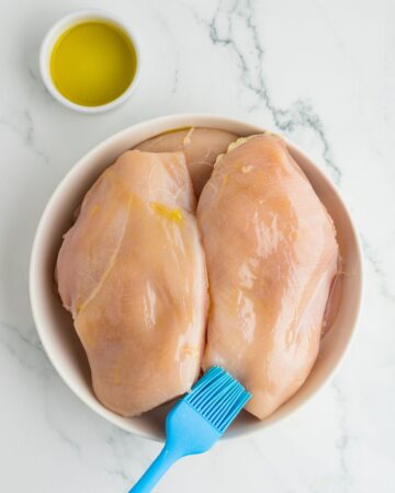 Boneless chicken breasts being rubbed with olive oil to make baked chicken breasts.