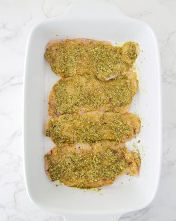 Pesto being brushed on chicken for a pesto chicken bake.
