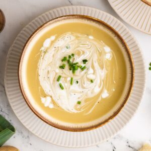 A bowl of potato leek soup, no cream topped with chopped chives and a swirl of sour cream.