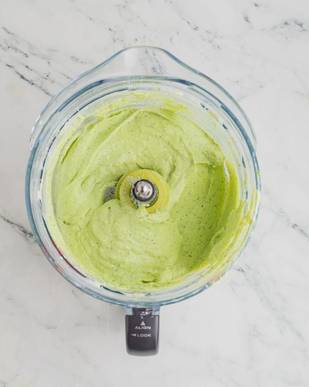 A food processor with ingredients to make Avocado Crema.