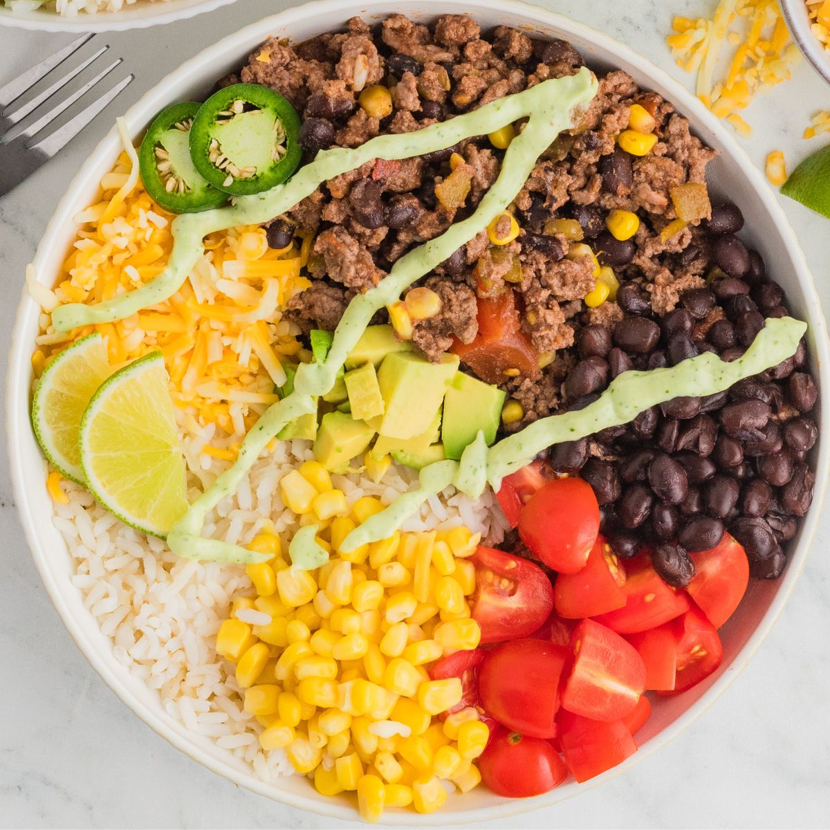 A beef burrito bowl with rice, corn, tomatoes, beans, and shredded cheese with an avocado crema.