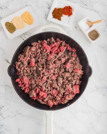 Ground beef browning in a cast iron pan to make easy beef burrito bowl recipe.