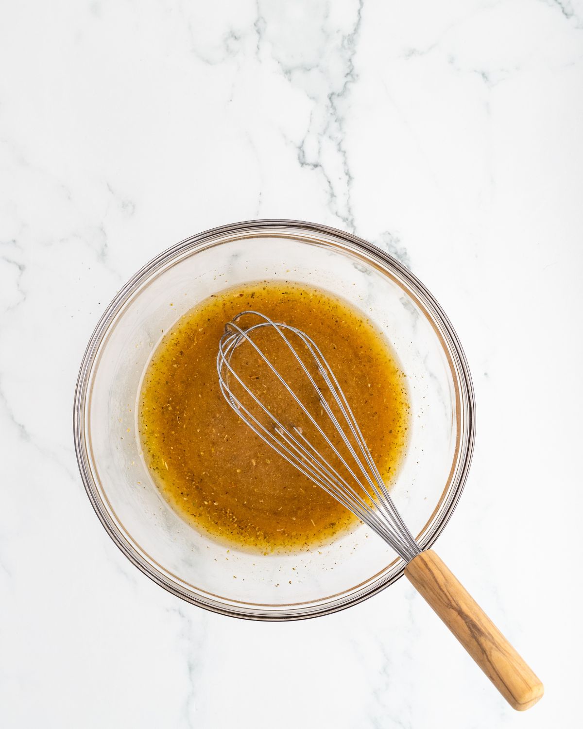 A glass bowl with a Greek marinade for a Greek Chicken Salad. 