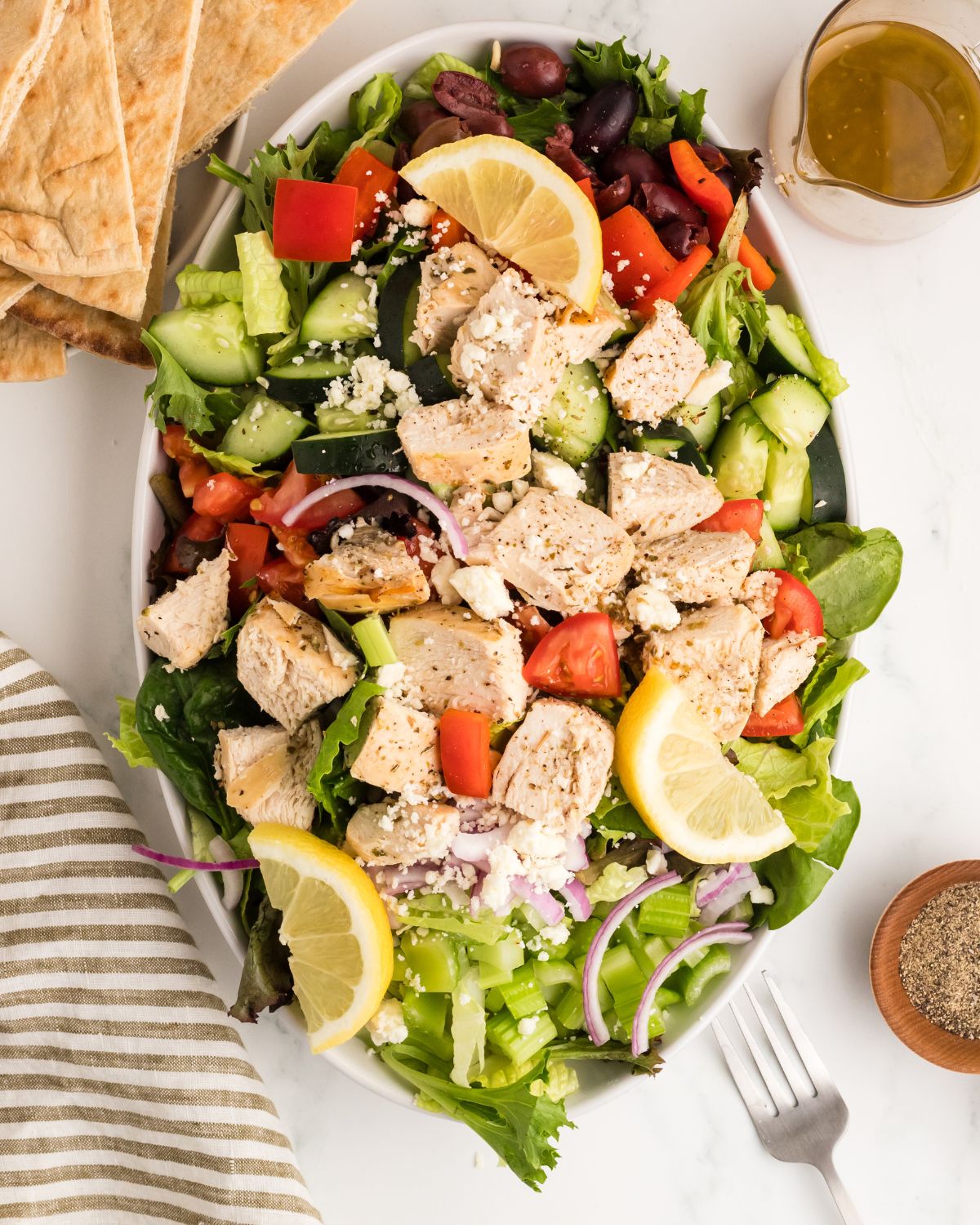 Greek Salad with chicken in a homemade Greek vinaigrette in an oval bowl with pita bread on the side.