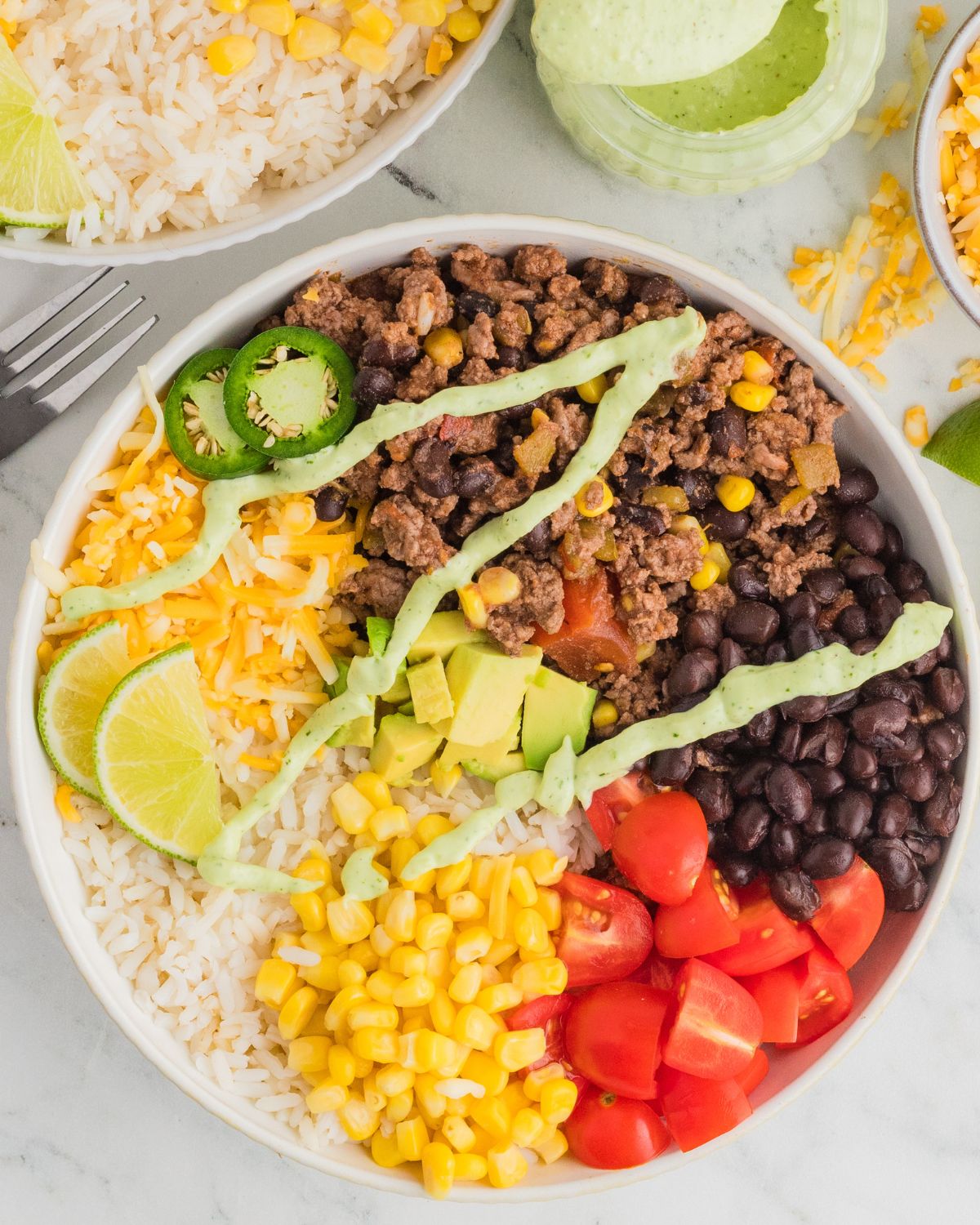A bowl of ground beef burrito bowls with seasoned ground beef, corn, beans and topped with an avocado crema.